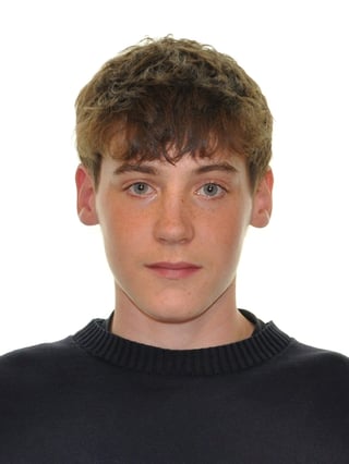 Portrait of a young man with brown hair and blue eyes wearing a black crew neck sweater against a white background